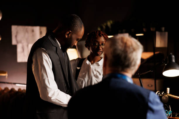Skilled tailors working on comissioned bespoke fitted premium quality suit for gentleman. Elegant client trying on custom made suit before suitmakers make necessary customizations